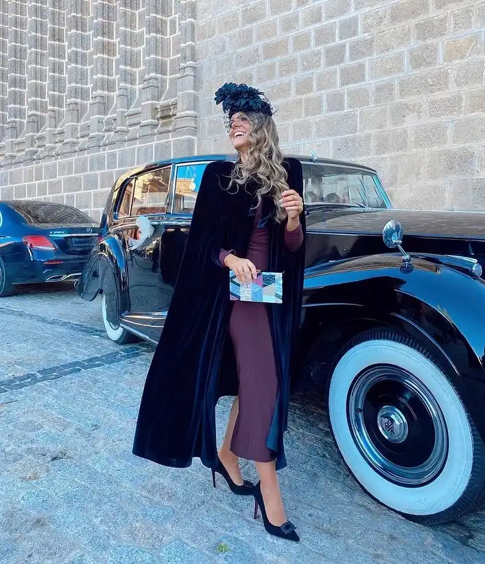 15 Winter Wedding Guest Outfits Over 40 That Handle the Cold 6 Black Velvet Cape Over a Plum Midi Dress