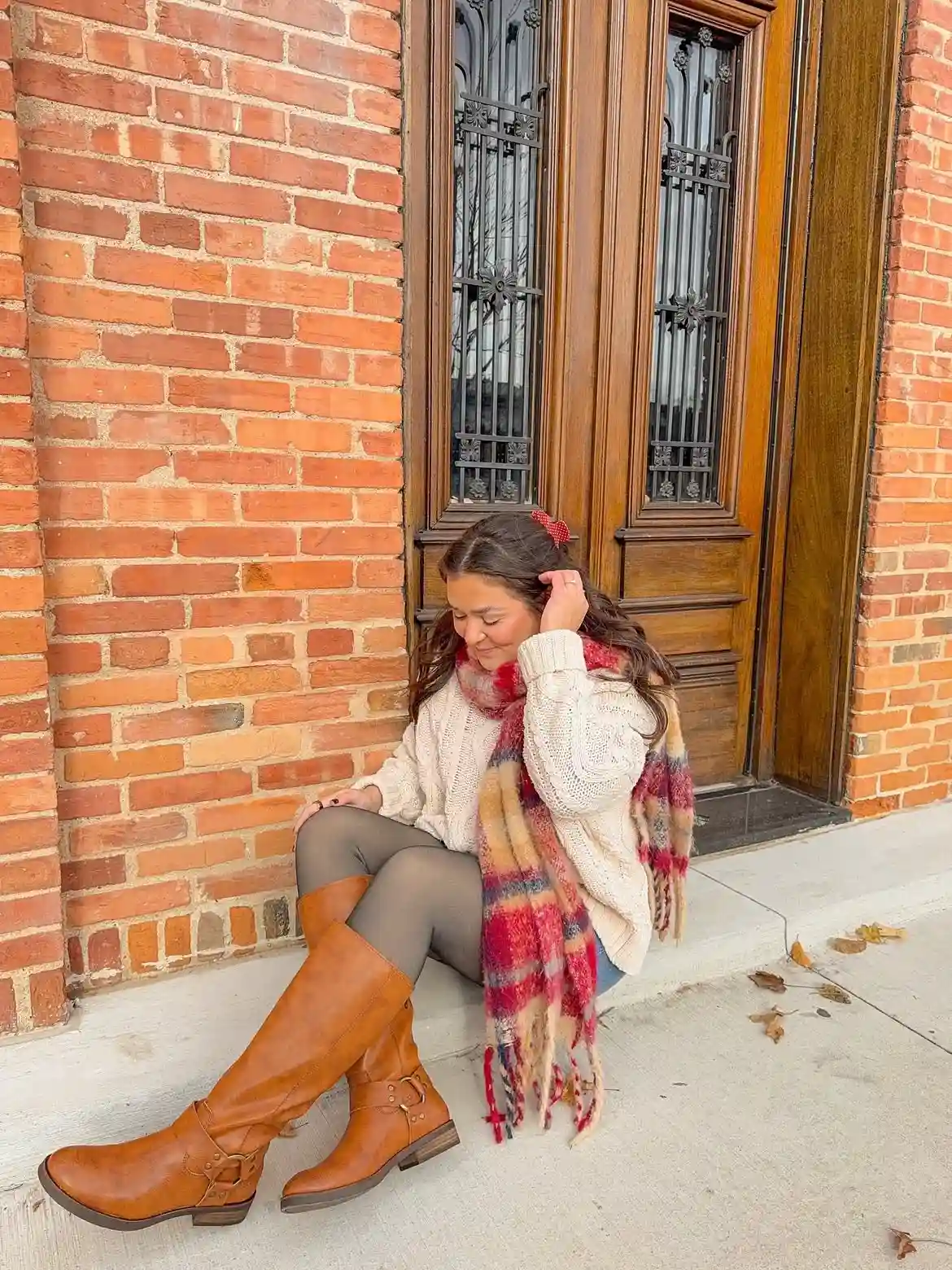 19 Winter Vacation Outfits Over 40 (Warm Getaways) 11 10. Cream Cable Sweater With a Plaid Scarf and Tall Boots