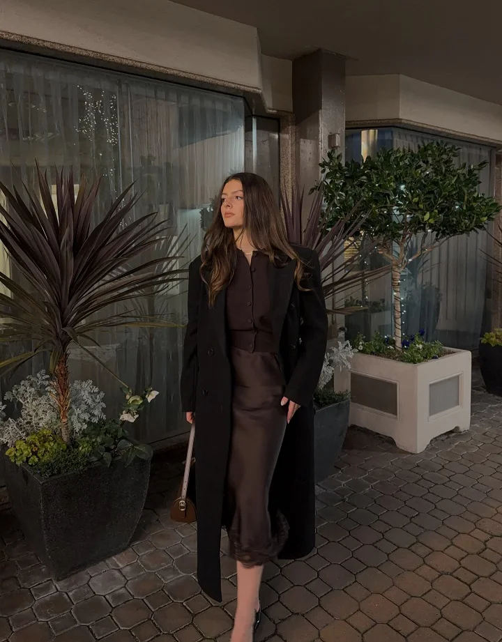 15 Fall Date Night Outfits Over 40 That Look Expensive Without Trying 12 11. Long Black Coat Over a Chocolate Satin Skirt Set